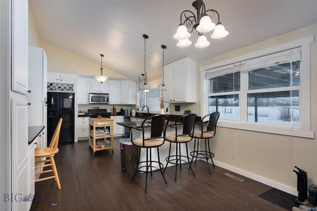 kitchen featuring dark countertops, a breakfast bar area, dark wood-style flooring, black appliances, and white cabinetry