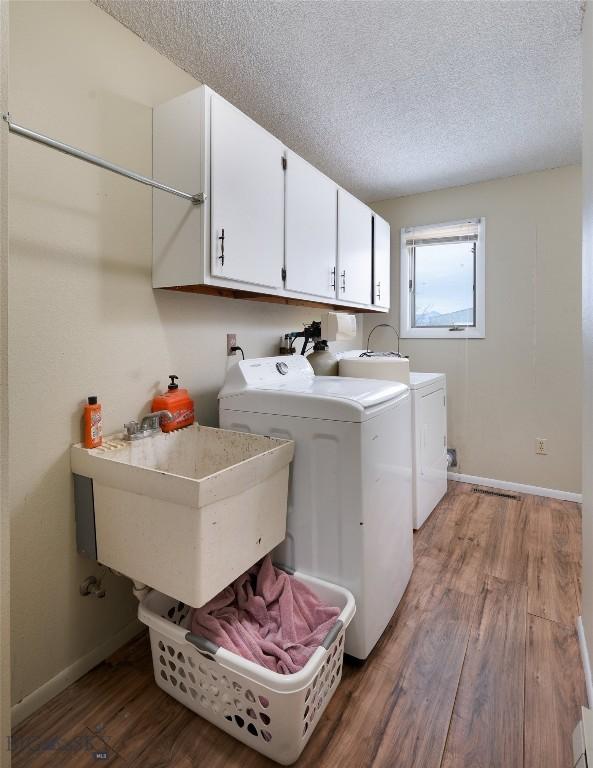 washroom with a textured ceiling, washer and clothes dryer, wood finished floors, and cabinet space