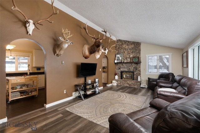 living area with dark wood-style floors, arched walkways, lofted ceiling, a stone fireplace, and a textured ceiling