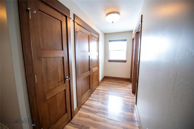 hallway featuring light wood finished floors and baseboards