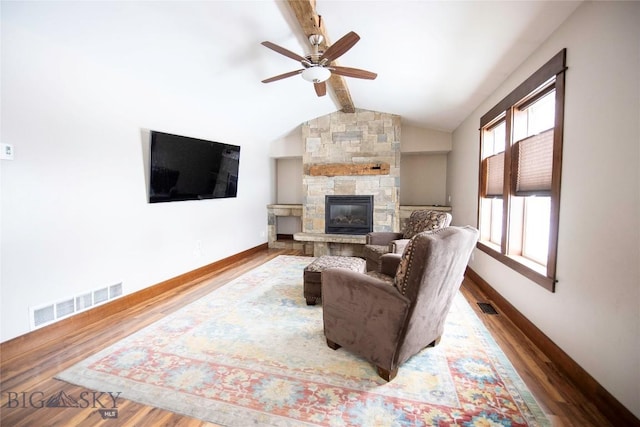 living area with baseboards, visible vents, lofted ceiling with beams, wood finished floors, and a stone fireplace