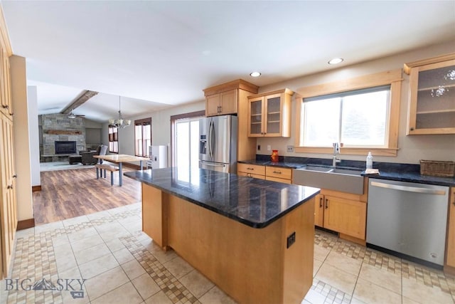 kitchen with vaulted ceiling with beams, light tile patterned floors, stainless steel appliances, a sink, and a stone fireplace