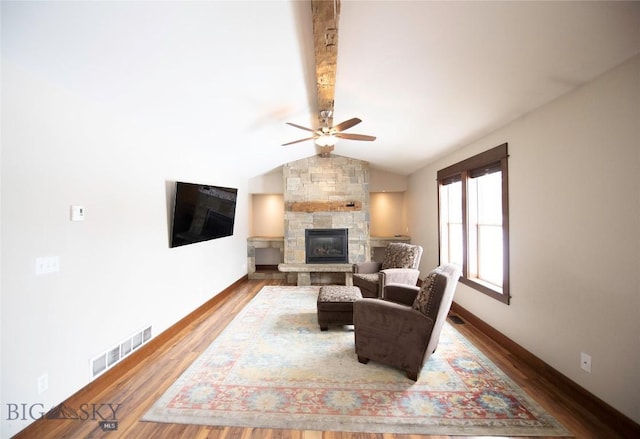 living room with baseboards, visible vents, lofted ceiling, wood finished floors, and a stone fireplace