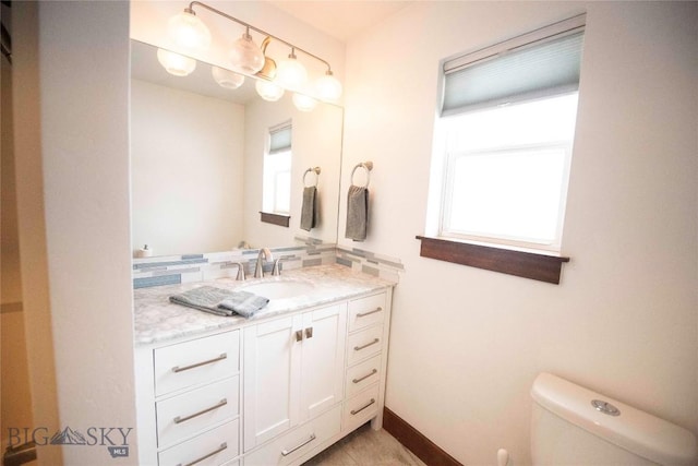 bathroom with toilet, plenty of natural light, baseboards, and vanity