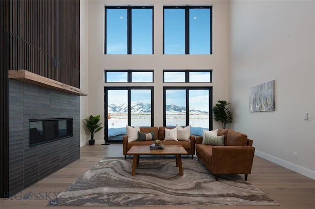 living room featuring a tile fireplace, a towering ceiling, baseboards, and wood finished floors