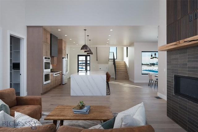 living area with baseboards, a glass covered fireplace, stairs, light wood-type flooring, and recessed lighting