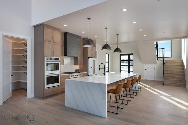 kitchen featuring white appliances, wall chimney exhaust hood, decorative backsplash, and light wood-style flooring