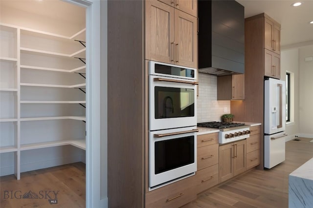 kitchen featuring light wood-type flooring, white appliances, wall chimney exhaust hood, and light countertops