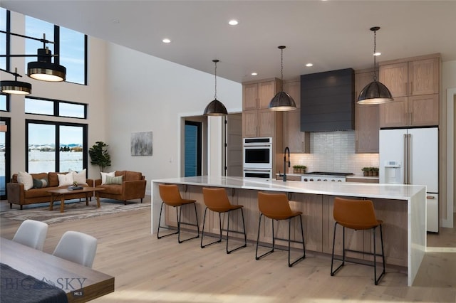 kitchen featuring light wood-type flooring, light countertops, white appliances, and premium range hood