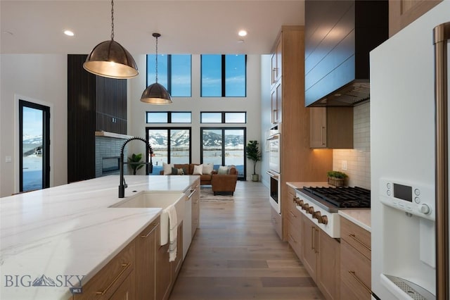 kitchen featuring white appliances, light wood-type flooring, tasteful backsplash, a glass covered fireplace, and custom range hood