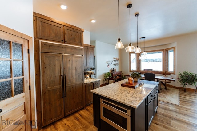 kitchen featuring built in appliances, light stone counters, a kitchen island, light wood-style floors, and pendant lighting