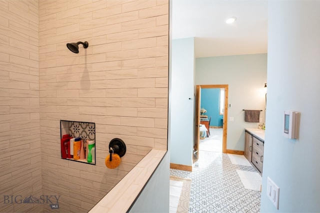 ensuite bathroom featuring connected bathroom, a tile shower, vanity, tile patterned flooring, and baseboards