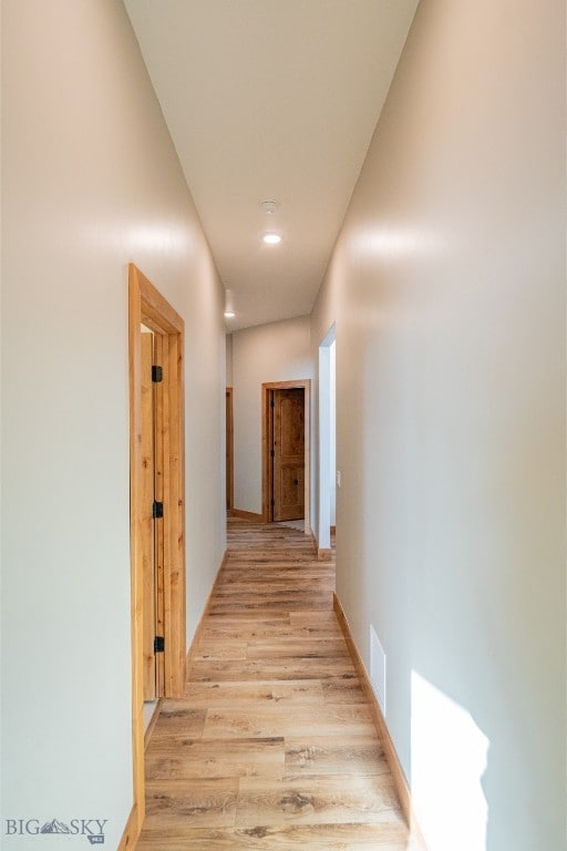 corridor with baseboards, visible vents, and light wood finished floors