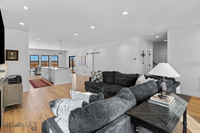 living area featuring a barn door, baseboards, light wood-style flooring, and recessed lighting