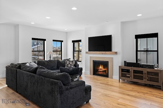 living room featuring wood-type flooring, a lit fireplace, baseboards, and recessed lighting