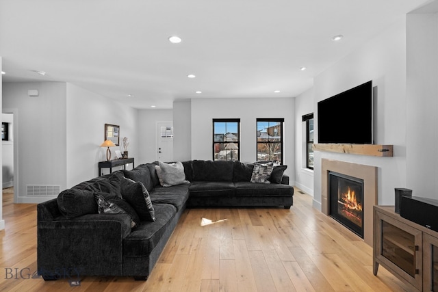 living area featuring light wood-type flooring, recessed lighting, visible vents, and a glass covered fireplace