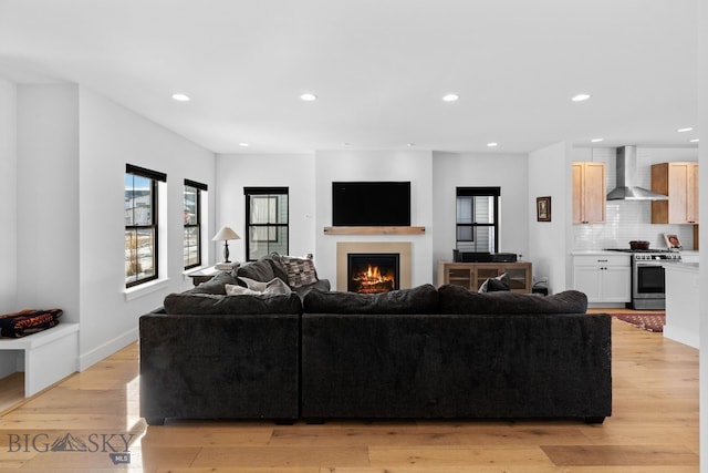 living area featuring light wood-style floors, a warm lit fireplace, baseboards, and recessed lighting