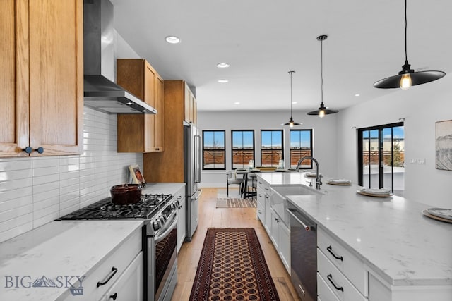 kitchen featuring tasteful backsplash, appliances with stainless steel finishes, a sink, wall chimney range hood, and light wood-type flooring