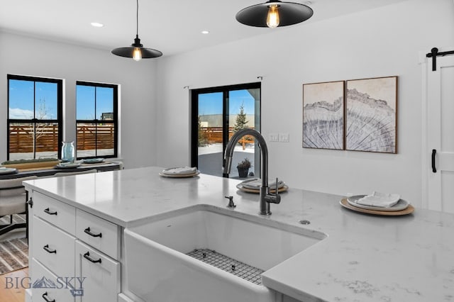 kitchen with light stone counters, a barn door, a sink, white cabinetry, and open floor plan