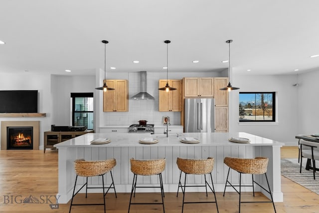 kitchen with stainless steel appliances, light wood-style floors, light countertops, wall chimney range hood, and tasteful backsplash