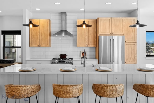 kitchen featuring stainless steel appliances, backsplash, decorative light fixtures, and wall chimney range hood