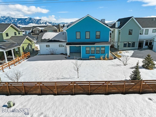 snow covered rear of property featuring a residential view, a mountain view, and fence private yard