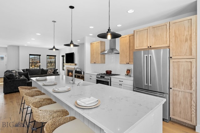 kitchen with stainless steel appliances, light wood-style flooring, wall chimney range hood, and light brown cabinetry