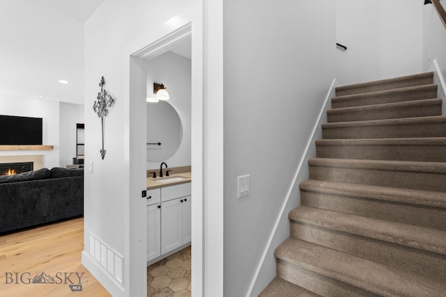 stairway with a lit fireplace, visible vents, wood finished floors, and recessed lighting