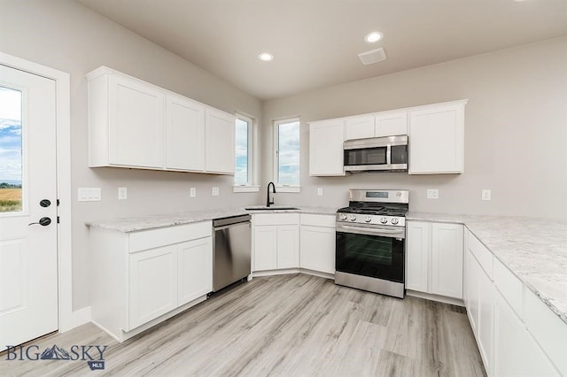 kitchen featuring appliances with stainless steel finishes, a sink, light wood-style flooring, and white cabinets