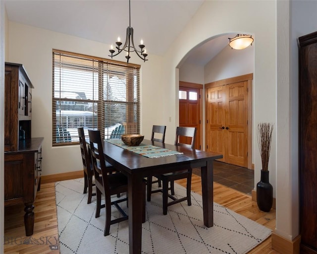 dining space featuring arched walkways, vaulted ceiling, a chandelier, light wood-type flooring, and baseboards