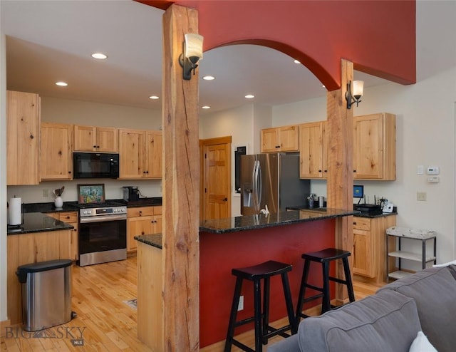 kitchen with arched walkways, a breakfast bar area, appliances with stainless steel finishes, light wood-style floors, and light brown cabinets