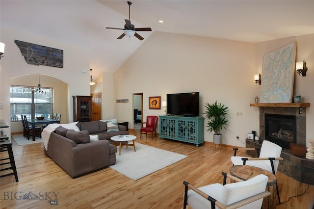 living room featuring ceiling fan, high vaulted ceiling, wood finished floors, baseboards, and a tiled fireplace