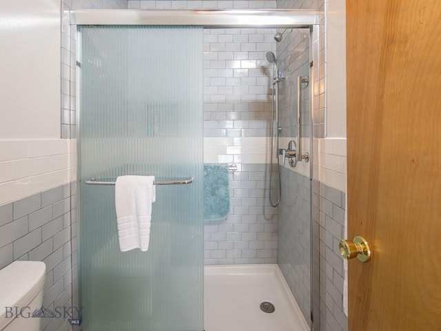 bathroom featuring a stall shower, tile walls, and toilet