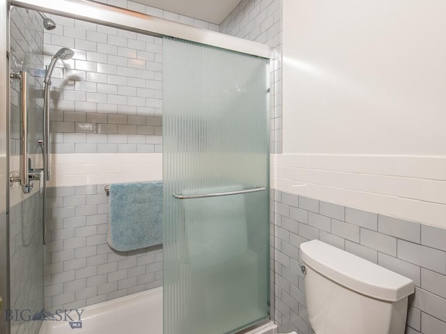 bathroom with tile walls, a shower stall, and toilet