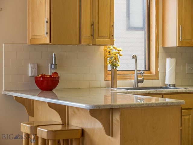 kitchen with tasteful backsplash, a breakfast bar area, light stone counters, and a sink