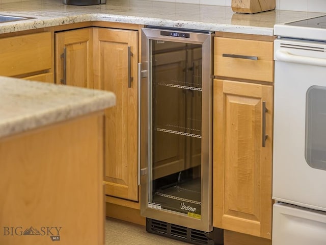 kitchen featuring beverage cooler, light brown cabinetry, light stone counters, and stove