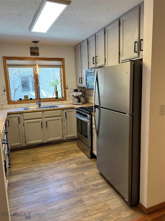 kitchen featuring stainless steel appliances, a sink, light countertops, and light wood-style floors