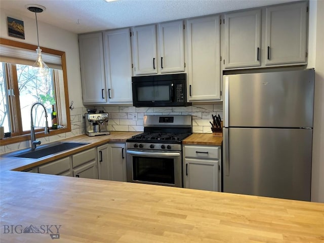 kitchen featuring stainless steel appliances, a sink, wooden counters, tasteful backsplash, and pendant lighting