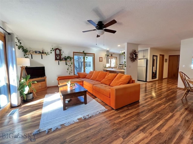 living area with ceiling fan, a textured ceiling, visible vents, and wood finished floors