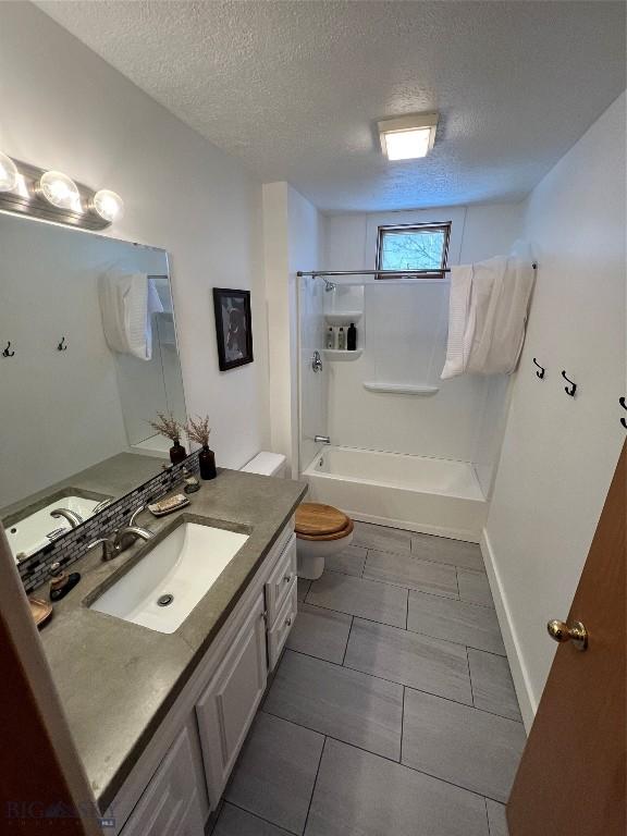 full bathroom with a textured ceiling,  shower combination, vanity, and toilet