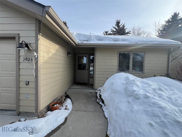 snow covered property entrance featuring an attached garage