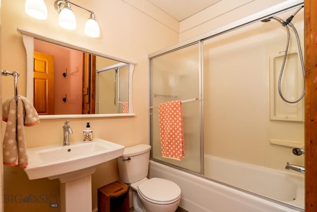 bathroom featuring toilet, bath / shower combo with glass door, and a sink