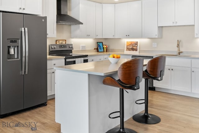 kitchen with stainless steel appliances, a sink, white cabinetry, wall chimney range hood, and a kitchen bar