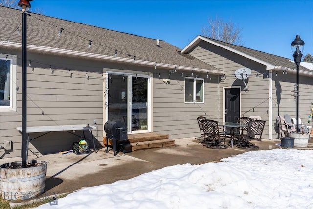 snow covered house with a shingled roof and a patio