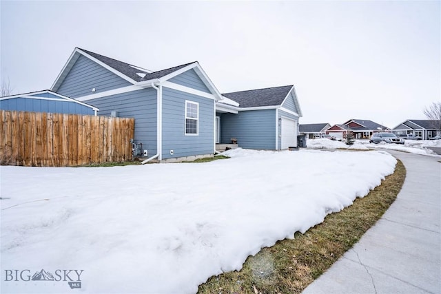 view of snowy exterior featuring a garage and fence