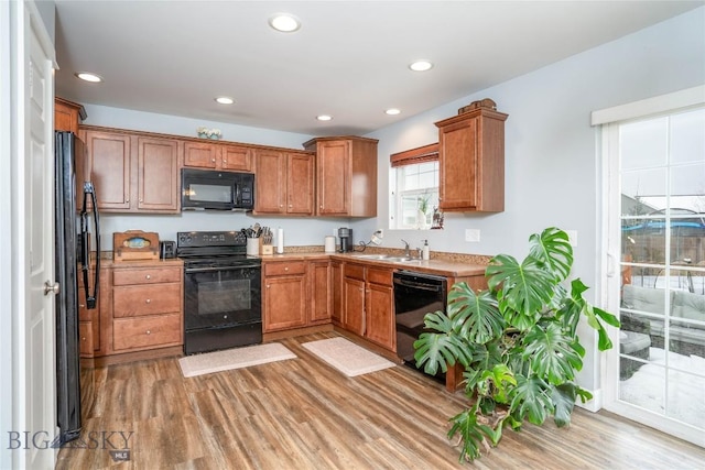 kitchen featuring light wood finished floors, brown cabinetry, black appliances, a sink, and recessed lighting