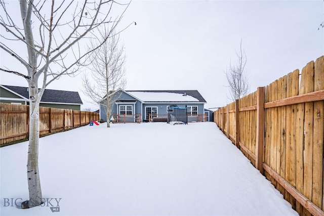 snow covered back of property featuring a fenced backyard and a deck