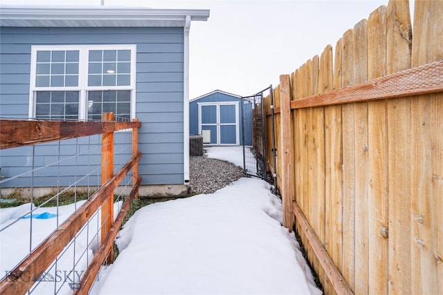 yard layered in snow featuring an outbuilding, a shed, cooling unit, and a fenced backyard