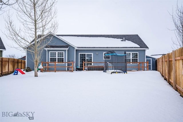 snow covered back of property featuring a deck, a storage unit, an outbuilding, and a fenced backyard