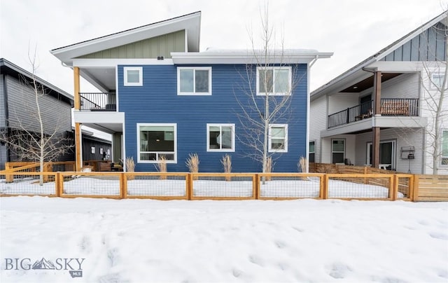 snow covered house with board and batten siding, a fenced front yard, and a balcony